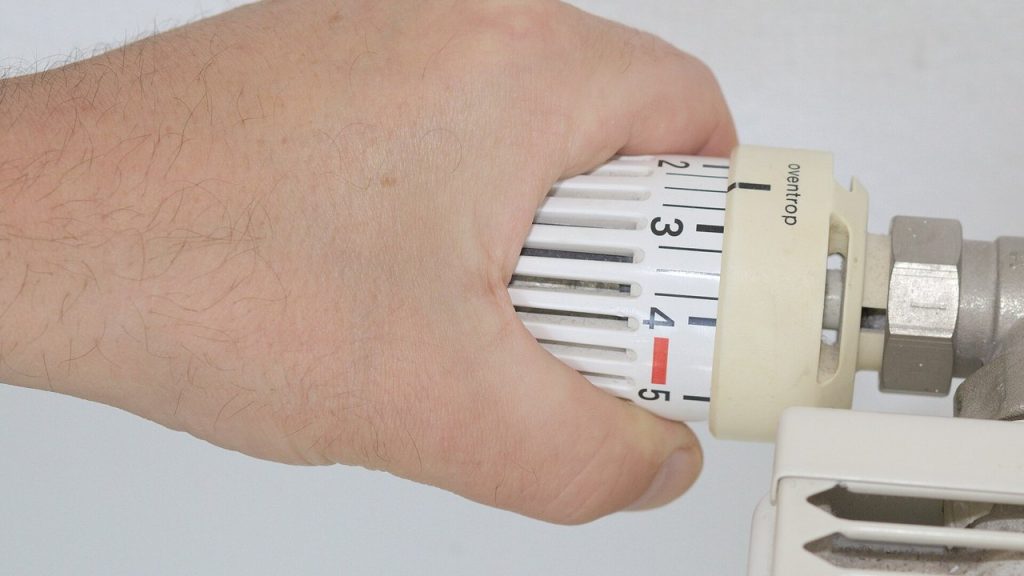 Heizperiode in der Mietwohnung: Ab wann muss der Vermieter heizen und wie warm muss es sein? Hand dreht das Thermostat eines Heizkörpers in einer Wohnung auf